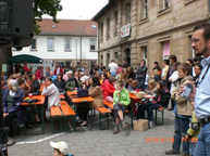 Das Publikum sitzt am Tag der offenen Tür unter schattigen Bäumen