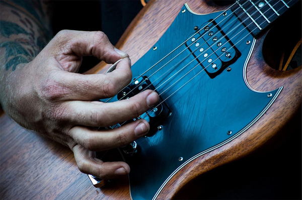 Hand mit Plektrum spielt E-Gitarre an